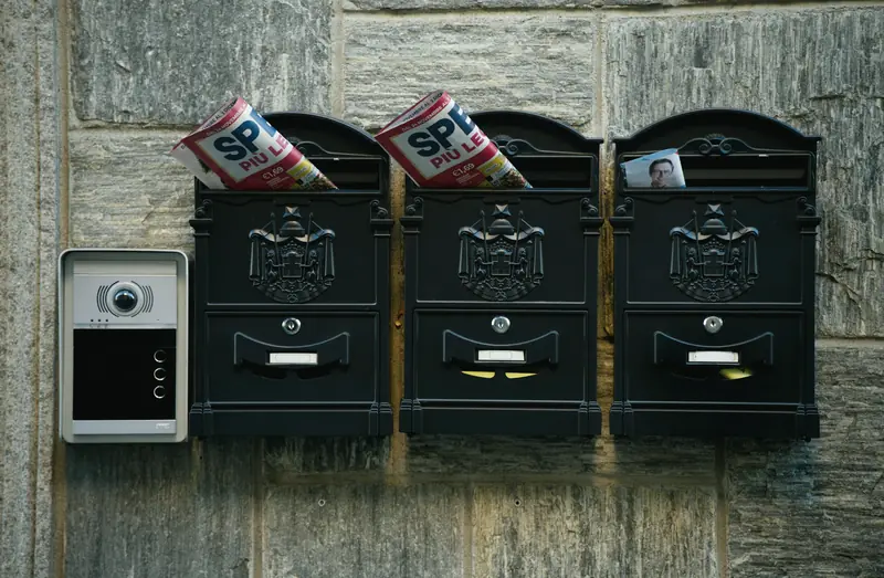 Drei schwarze Briefkästen neben einer Türklingel mit Kamera an einer Steinwand
