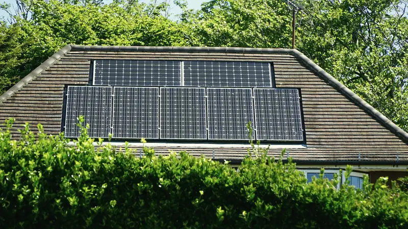 Wohnhaus mit Solarmodulen auf dem Walmdach hinter einer Hecke (Symbolbild)